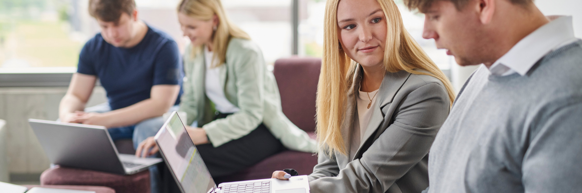 Eine Gruppe von Studierenden arbeitet gemeinsam an Laptops, während sie sich über digitale Lösungen wie das Unterschreiben einer Hausarbeit austauschen.