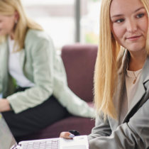 Eine Gruppe von Studierenden arbeitet gemeinsam an Laptops, während sie sich über digitale Lösungen wie das Unterschreiben einer Hausarbeit austauschen.