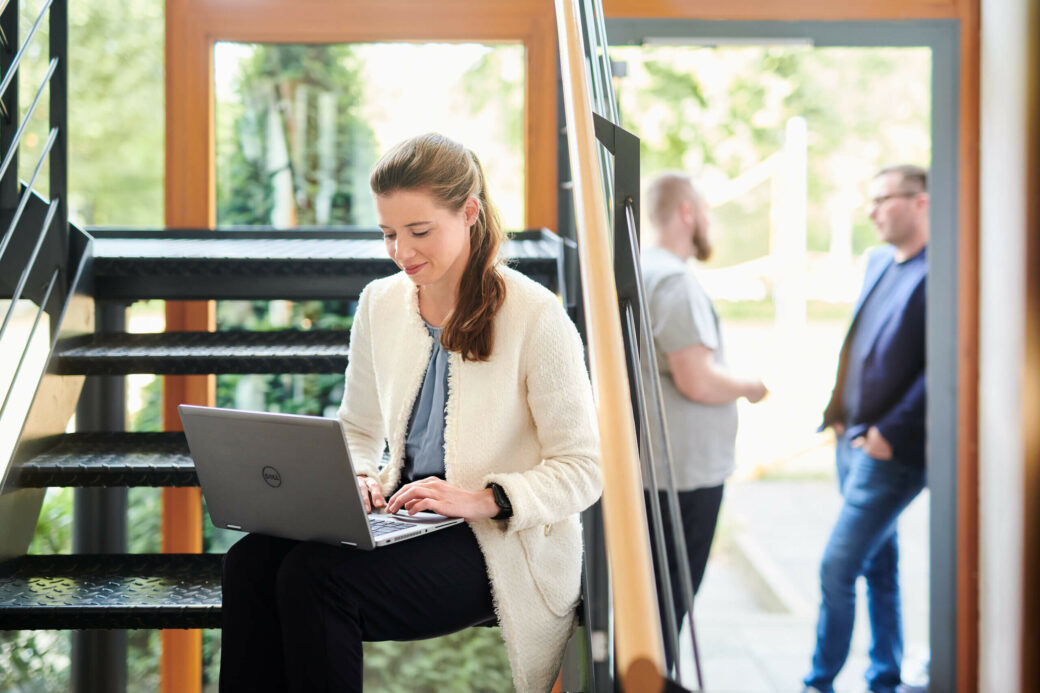 Frau mit Laptop sitzt auf einer Treppenstufe im Foyer des Unternehmens