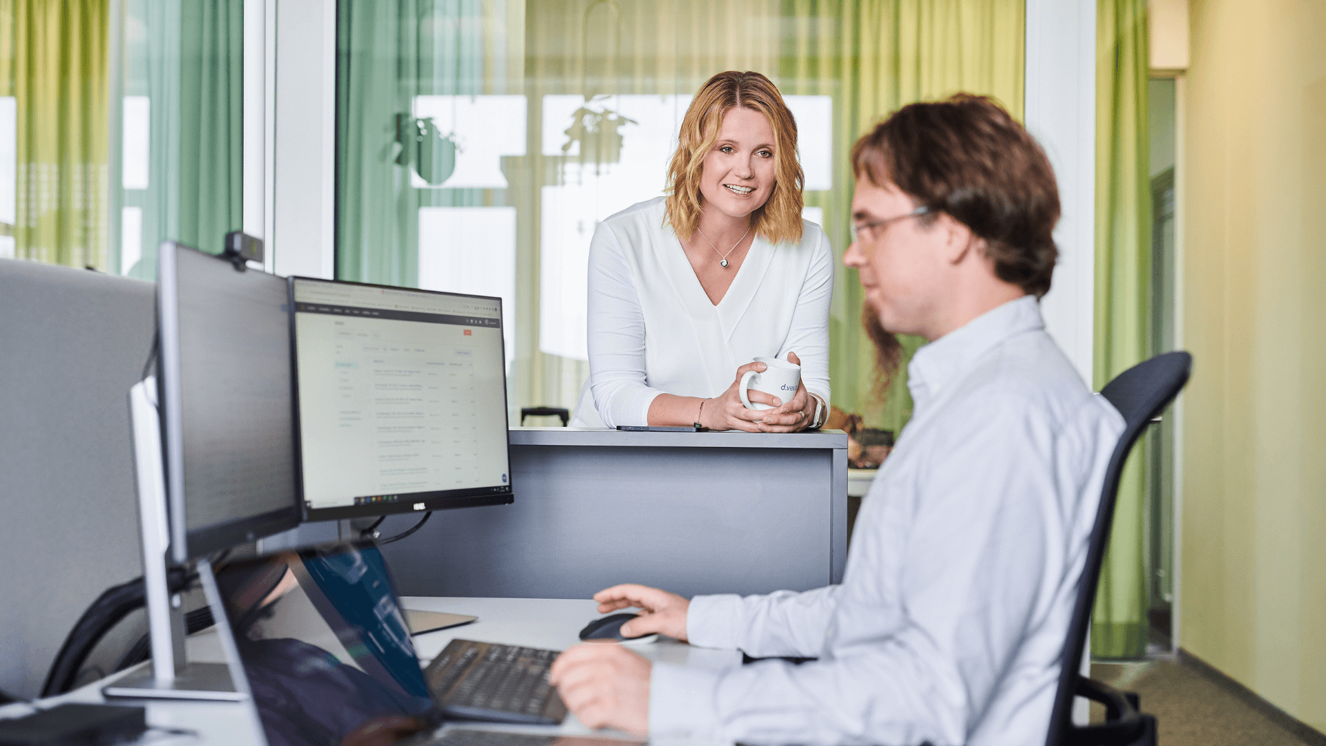 Gespräch unter Mitarbeitenden im Büro: Frau spricht mit Mann am PC