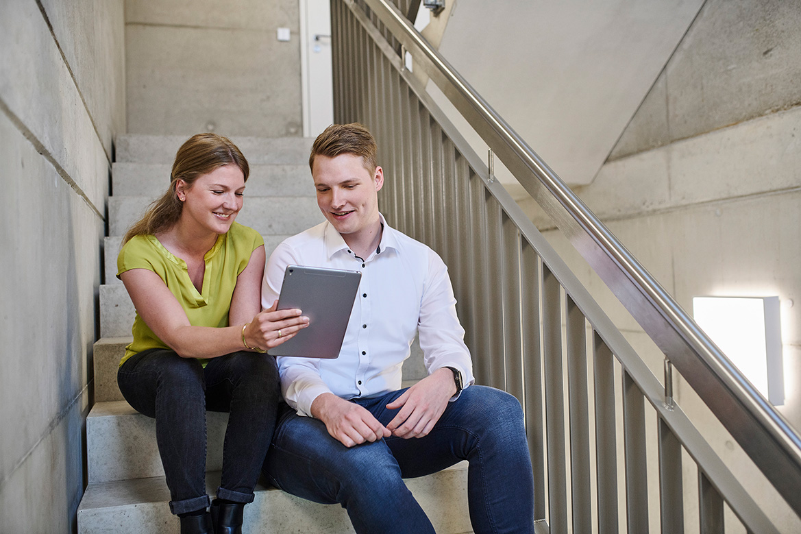 Zwei Mitarbeiter sitzen auf einer Treppe und schauen sich auf dem Tablet eine elektronische Signatur an