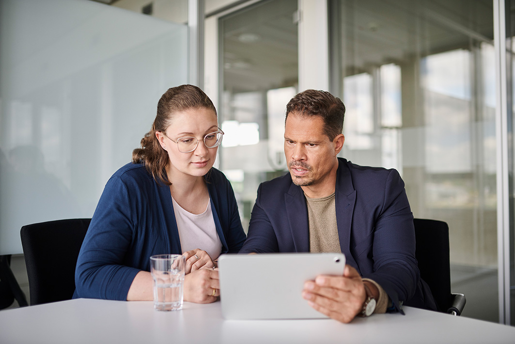 Zwei Mitarbeiter sitzen am Tisch und schauen sich eine elektronische Signatur Software auf dem Tablet an