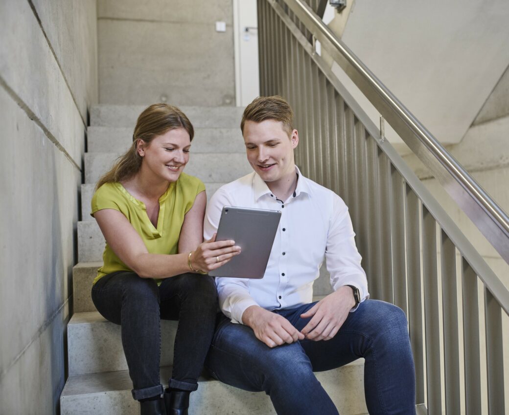 Zwei Personen sitzen auf einer Treppe und halten ein Tablet in der Hand