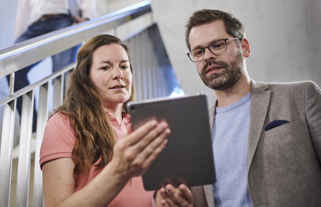 Eine Frau und ein Mann schauen auf ein Tablet, auf dem die Stadtwerke-App angezeigt wird, die die benutzerfreundliche Oberfläche und Funktionen der App zeigt, einschließlich personalisierter Einstellungen und relevanter Dienstleistungen